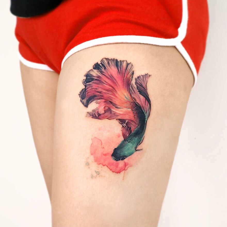 Painting-like tattoo of a colorful fish on a person's thigh, showcasing intricate artistic detail.