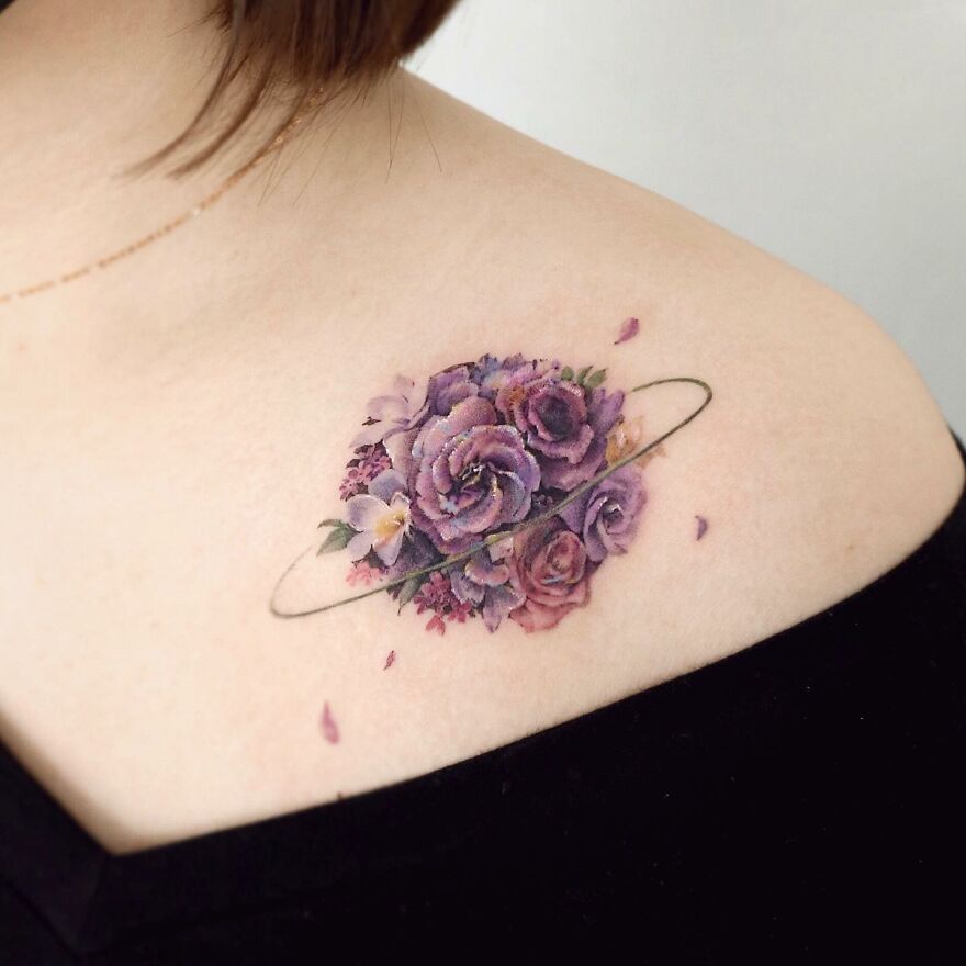 Painting-like tattoo of purple flowers and rings on a person's shoulder, showcasing intricate artistry and detail.