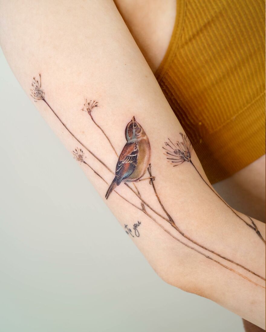 Painting-like tattoo of a bird on a branch, intricately designed on an arm.