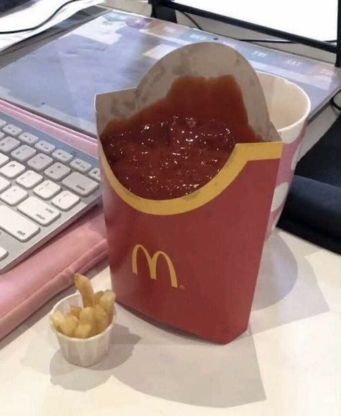 Cursed food with fries container filled with ketchup, tiny fries in a paper cup beside a keyboard.