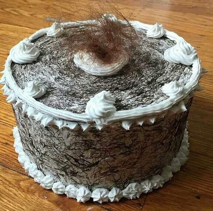 Cursed food: cake decorated with hair-like patterns and dollops of frosting on a wooden surface.