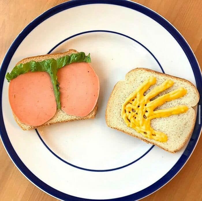Cursed food featuring sandwich with bologna and lettuce on one side and mustard handprint on the other.