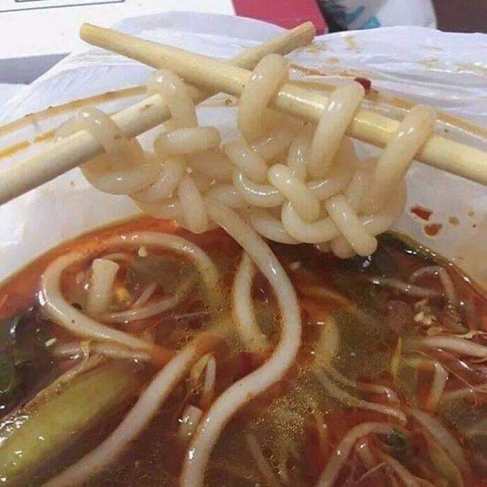 Cursed food: knotted noodles on chopsticks in spicy soup.
