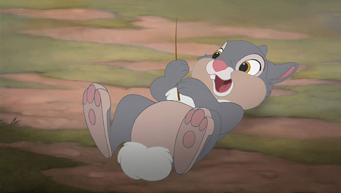 Cute animated character, a grey rabbit, lying on its back and holding a stick with a joyful expression.