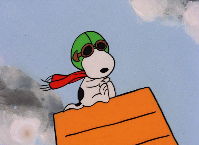 Cute animated character in aviator goggles and helmet atop a doghouse, wearing a red scarf against a blue sky backdrop.