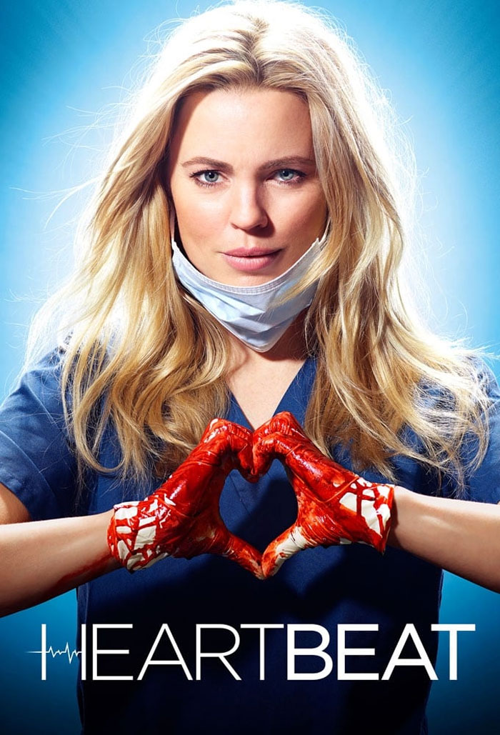 Doctor in scrubs with a face mask making a heart gesture with bloody gloves, promoting medical drama TV show "Heartbeat".