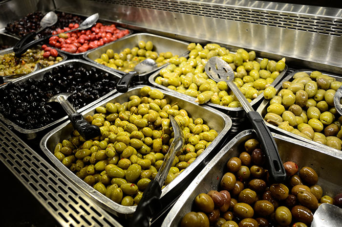 Variety of olives displayed in metal trays at a food market showcasing some of the most inedible foods.