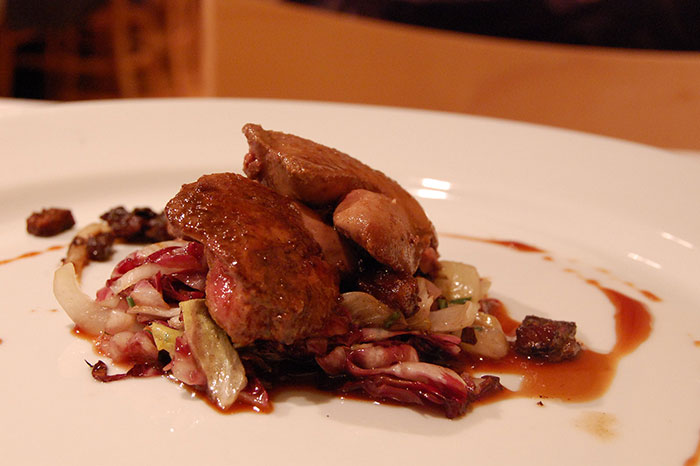 Close-up of plated inedible food with cooked meat and mixed greens drizzled with sauce on a white dish.