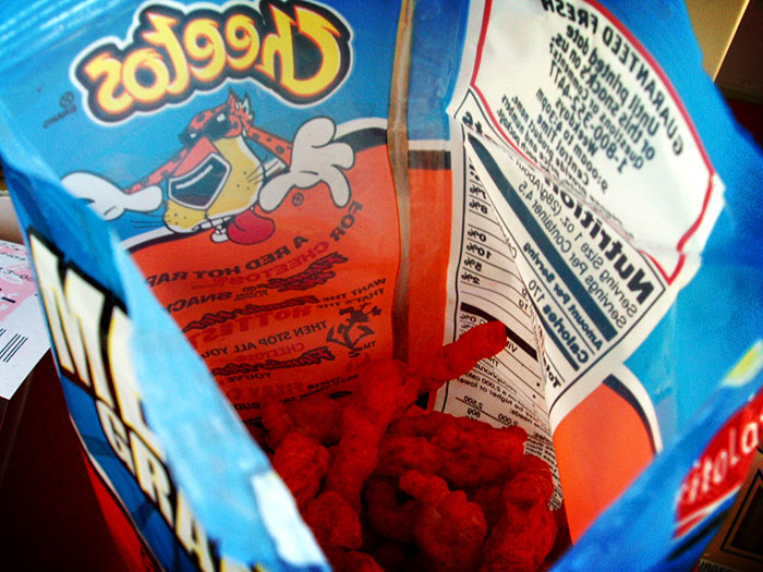 Open bag of spicy Cheetos snacks showing bright red chips and nutrition label, representing inedible foods.
