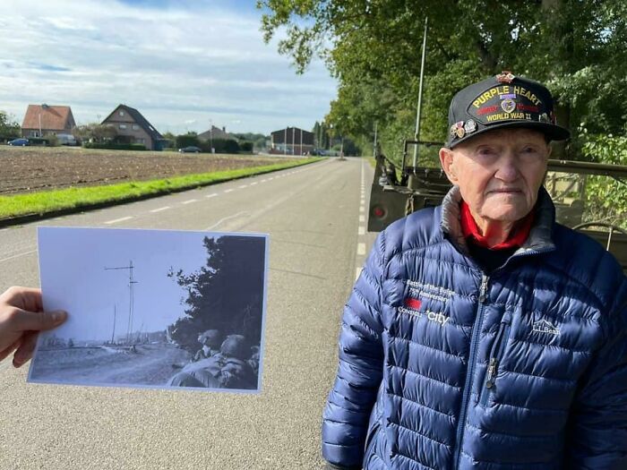 Elderly man holds WWII photo at the same location, showing time's effect on the scenery.