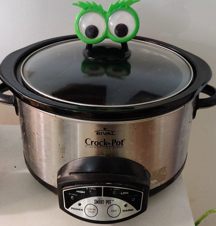 Slow cooker with green wiggle eyes on lid creating a playful eyebombing effect on a kitchen countertop.