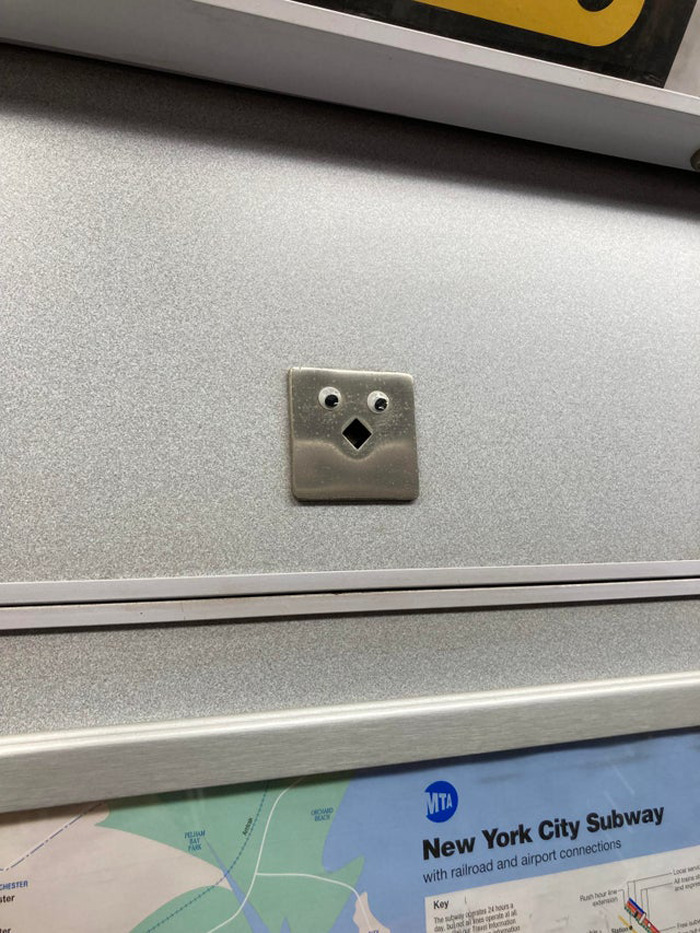 Metal panel on subway wall decorated with wiggle eyes, enhancing random objects as seen in eyebombing community posts.