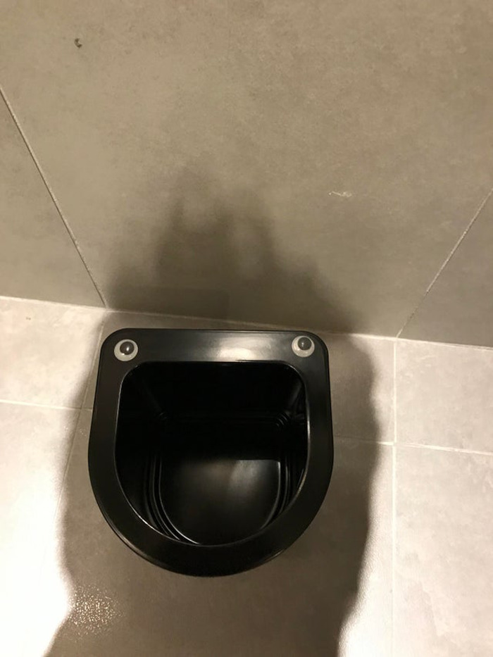 Black trash bin with wiggle eyes attached, making it look like a face, showcasing creative eyebombing on a tiled floor.