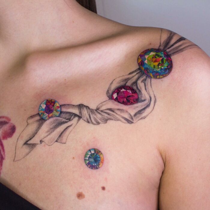 Colorful gemstone tattoo resembling permanent jewelry on shoulder.