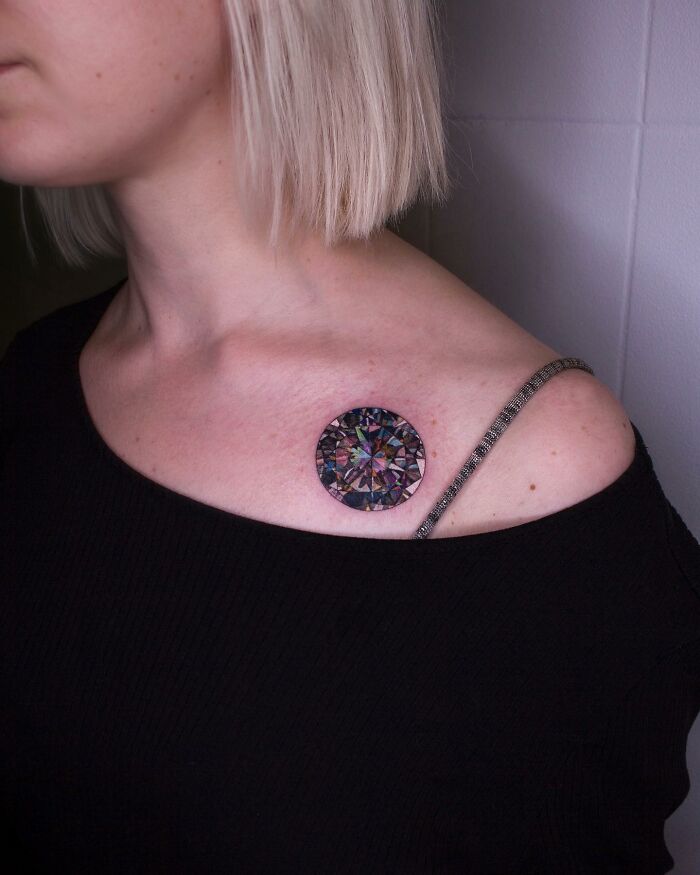 Colorful "permanent jewelry" tattoo on a woman's shoulder, resembling a gemstone design.