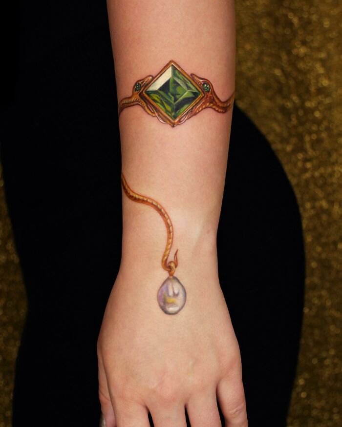 Arm adorned with permanent jewelry tattoo featuring a gemstone and chain design.