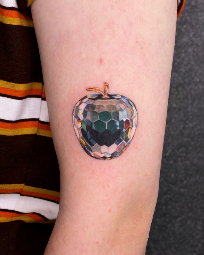 Colorful geometric apple tattoo on a person's arm, representing permanent jewelry.