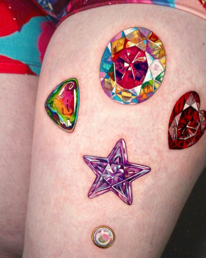 Vibrant "permanent jewelry" tattoos on skin, featuring colorful gem designs including a star and various shapes.