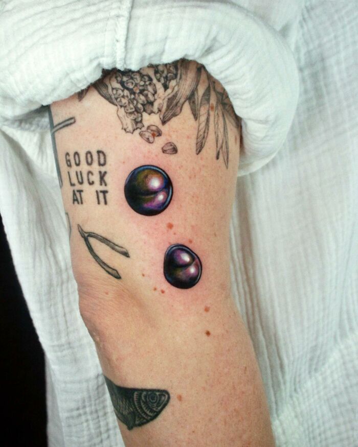 Arm with "permanent jewelry" tattoo featuring colorful spheres, wishbone, and text.
