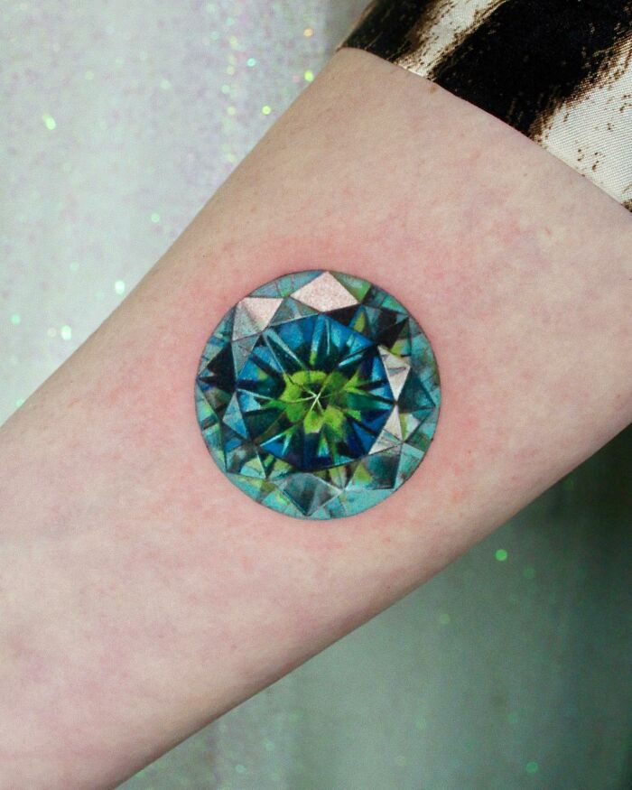 Colorful gemstone tattoo resembling a permanent jewelry design on a forearm.