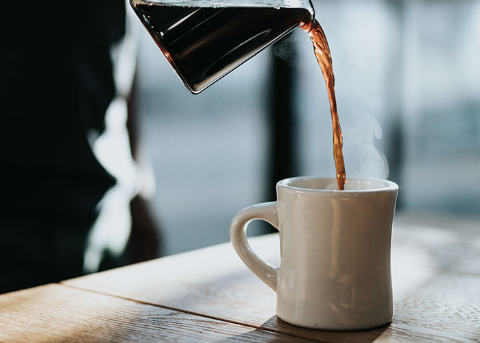 Pouring hot coffee into a white mug in a kitchen, illustrating secret things people do in their kitchen.