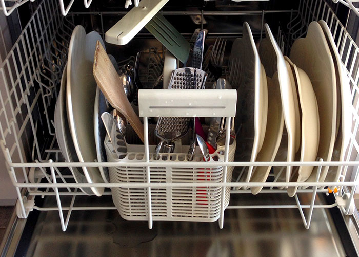 Dishwasher loaded with plates, cooking utensils, and kitchen tools illustrating secret kitchen habits people reveal.