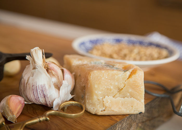 Close-up of garlic cloves and a block of cheese on a wooden board showing kitchen secrets and unique food preparation habits.