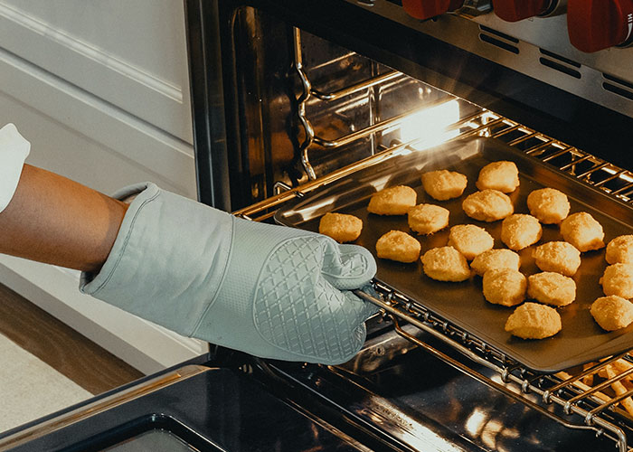 Person wearing an oven mitt placing a tray of nuggets into the oven, highlighting secret things done in their kitchen.