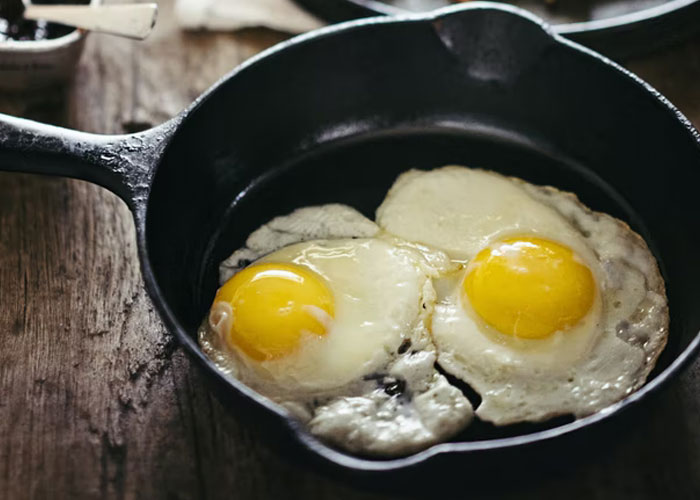 Cast iron skillet with two sunny side up eggs cooking on a wooden surface, revealing secret kitchen habits.