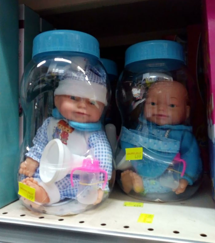 Two creepy baby dolls in blue outfits inside jars with blue lids, displayed on a store shelf as creepy toys.