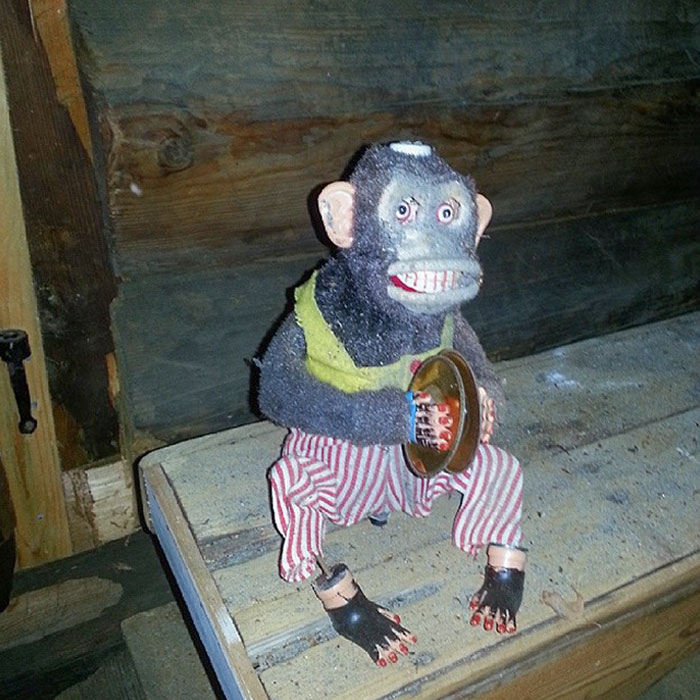 Creepy vintage toy monkey with cymbals wearing striped pants and a yellow vest on a wooden surface.