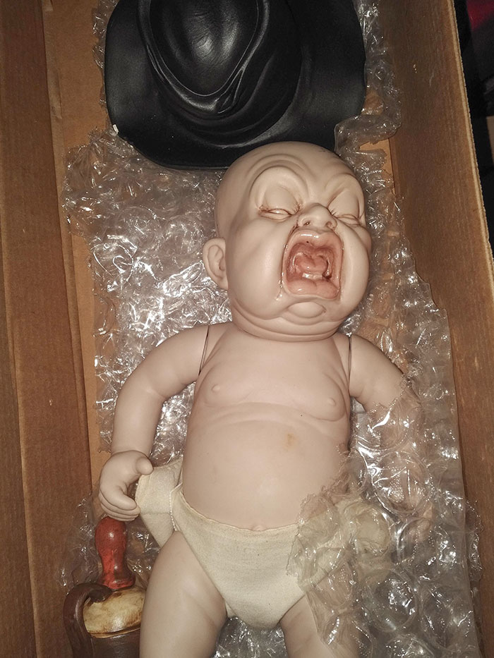Creepy toy baby doll with exaggerated screaming expression lying in a box with bubble wrap, unsettling and nightmare-inducing.