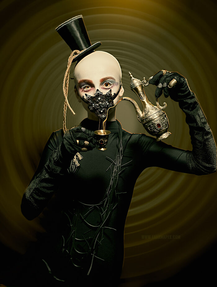 Dark Alice character in a surreal costume, wearing a top hat and mask, holding a teapot and cup against a swirling backdrop.