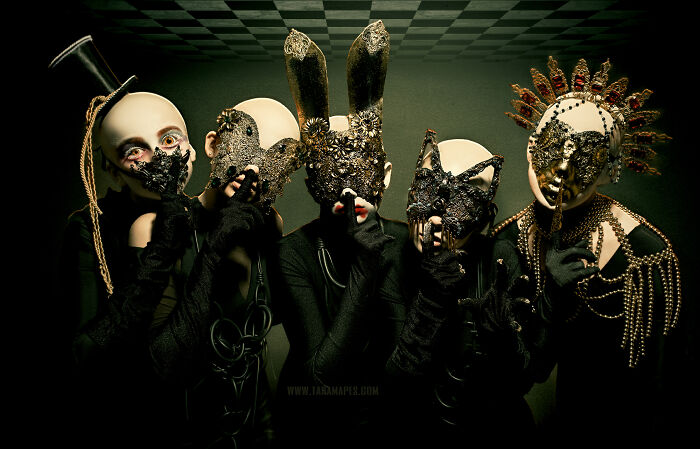 Dark Alice interpretation with four masked figures, each wearing elaborate costumes, embodying a surreal and mysterious theme.