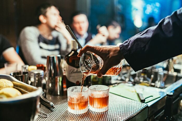 Bartender pouring whiskey into glasses at a bar with blurred guests in the background at a wedding reception.