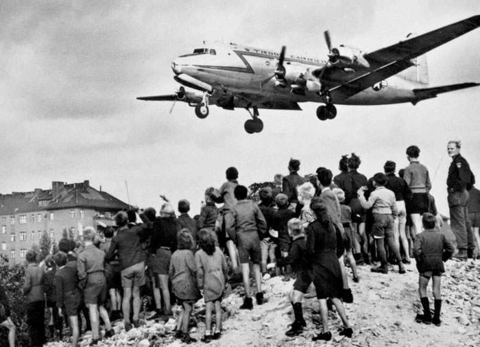 Group of children and adults watching a historic plane landing, symbolizing unexpected acts of kindness in history.