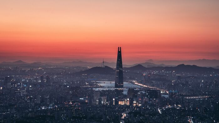 Seoul city skyline at sunset with Lotte World Tower and surrounding mountains, showcasing beautiful urban landscape.
