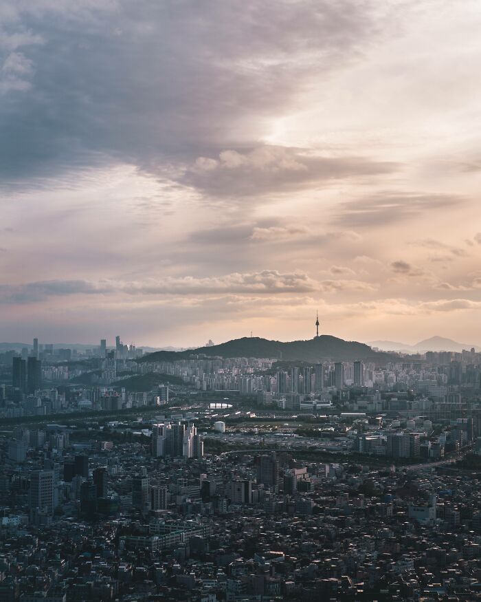 Seoul cityscape at dusk with urban buildings and Namsan Seoul Tower under a cloudy sky.