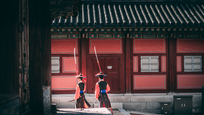 Two traditional guards in colorful uniforms standing in front of a historic building in Seoul, a beautiful city in South Korea.