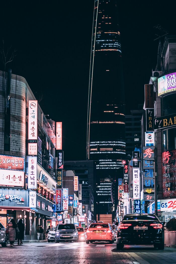 Night street scene in Seoul with brightly lit signs and the city’s skyscrapers towering in the background.
