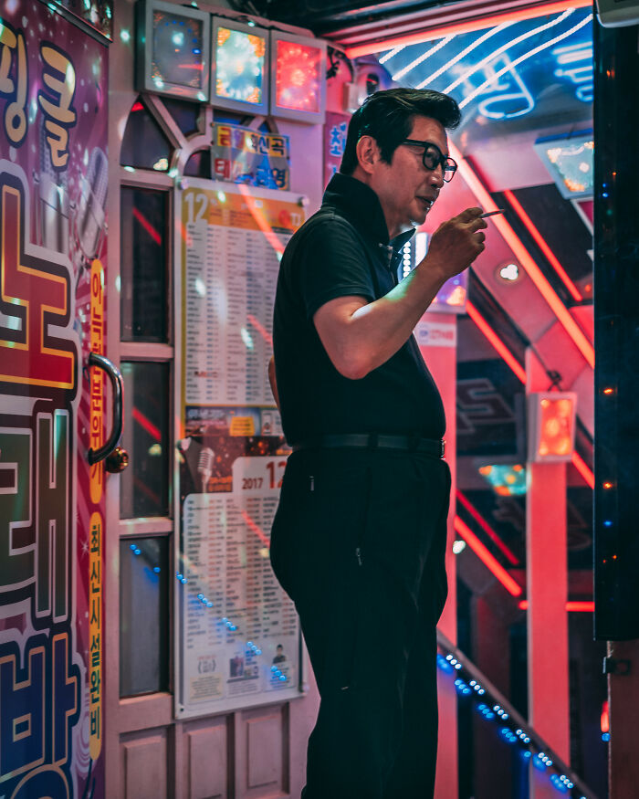 Man smoking outside a colorful karaoke bar lit with neon signs in Seoul, showcasing the city's vibrant nightlife.