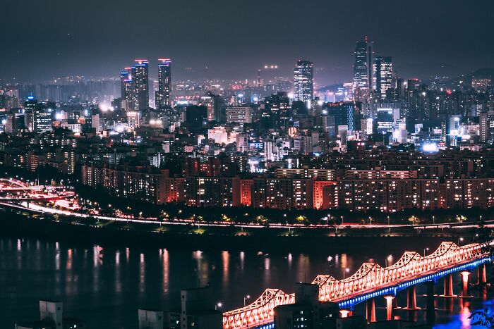 Nighttime cityscape of Seoul with illuminated skyscrapers and a glowing bridge over the river, showcasing beautiful Seoul city views.