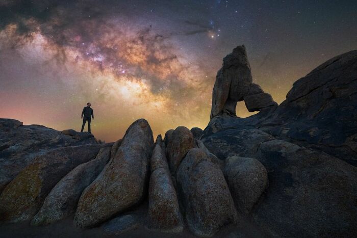 Person standing on rock formation under a stunning nightscape sky with visible Milky Way.