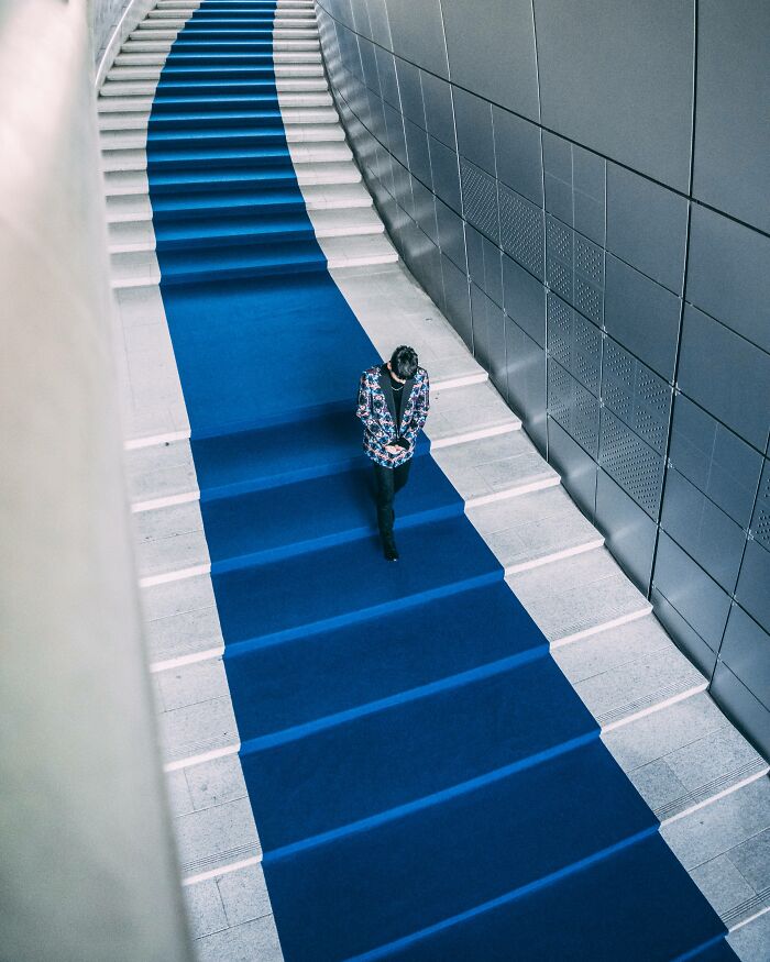 Person walking down wide stairs with a blue carpet in a modern urban setting, showcasing Seoul's unique cityscape.