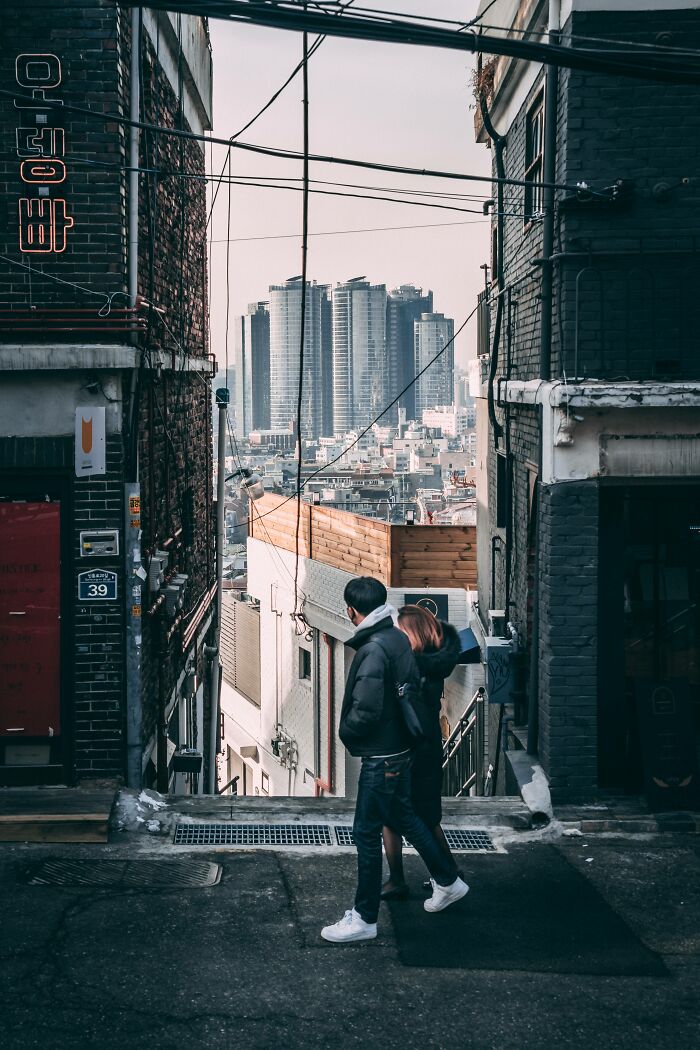 Couple walking through narrow alley in Seoul with modern skyscrapers in the background showcasing the beautiful cityscape.
