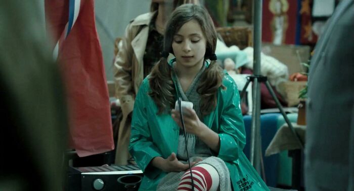 Young girl in a green raincoat using a mobile phone, sitting among movie props revealing hidden details from popular films.