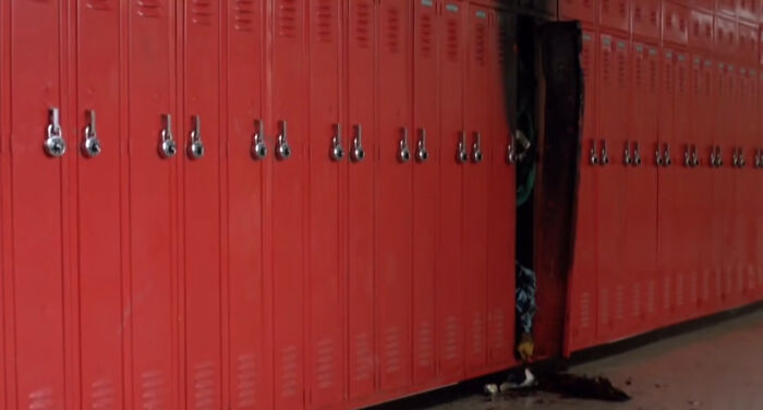 Red school lockers with one locker open slightly, revealing a dark interior and debris on the floor, Easter eggs from popular films.
