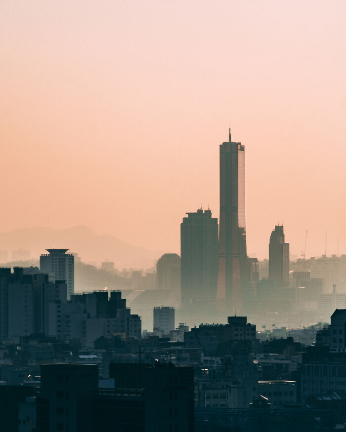 Seoul city skyline during sunset with tall buildings and soft orange sky, showcasing beautiful urban landscape.