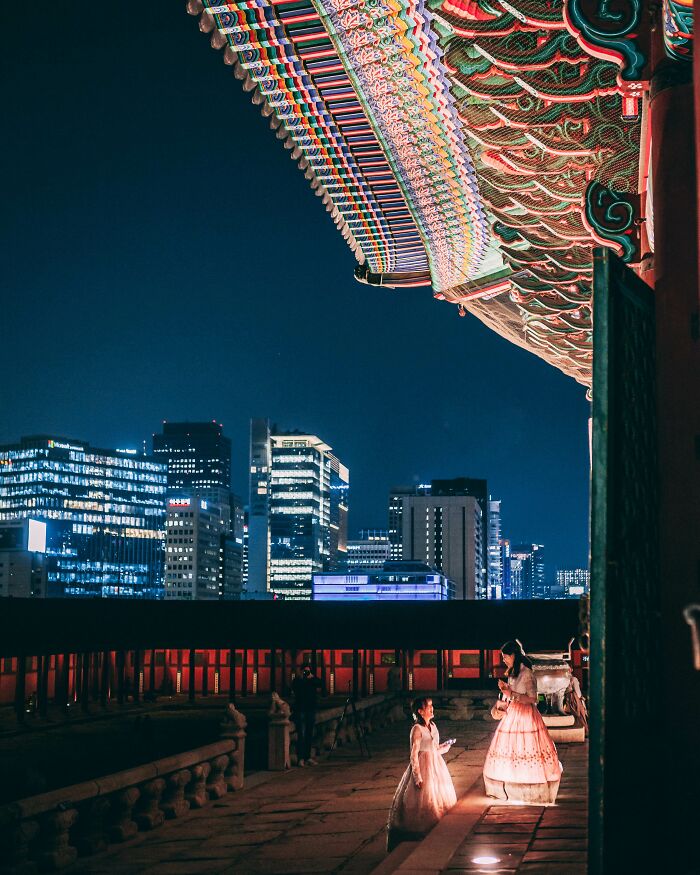 Traditional Korean architecture roof details with two women in hanbok in Seoul city nightscape, highlighting Seoul beauty.