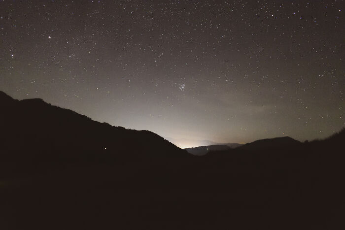 Starry night sky over dark silhouettes of the Ukrainian Carpathians mountains with a faint glow on the horizon.